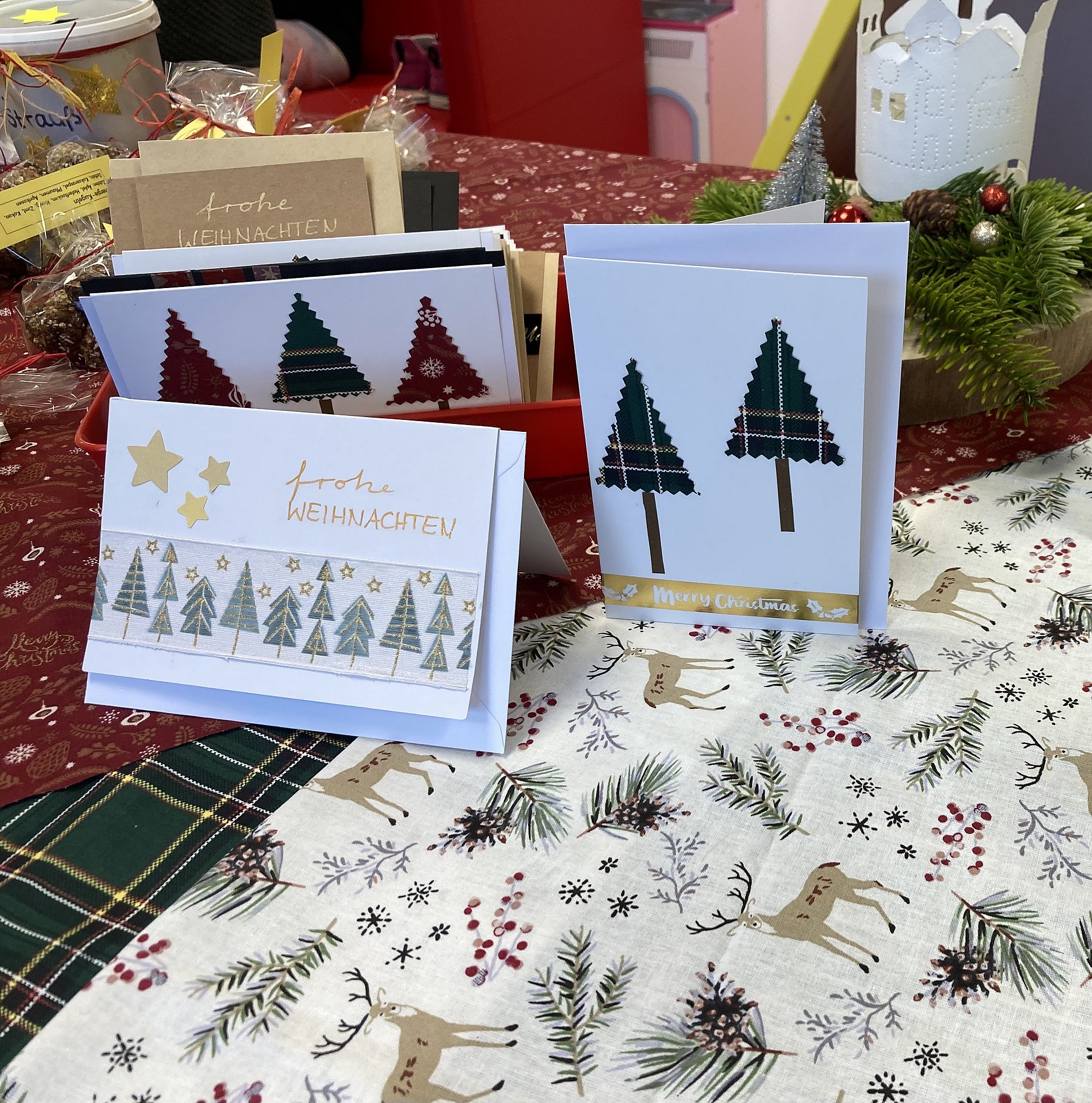 Auf einem weihnachtlich gedeckten Tisch stehen Weihnachtskarten mit Tannenbaum Motiven