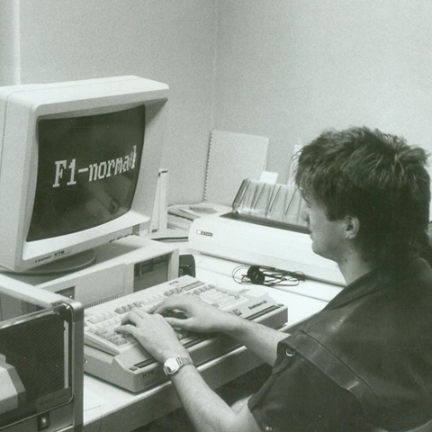 Eine schwarz weiß Fotografie. Ein Mann sitzt an einem Computer und gibt etwas in die Tastatur ein
