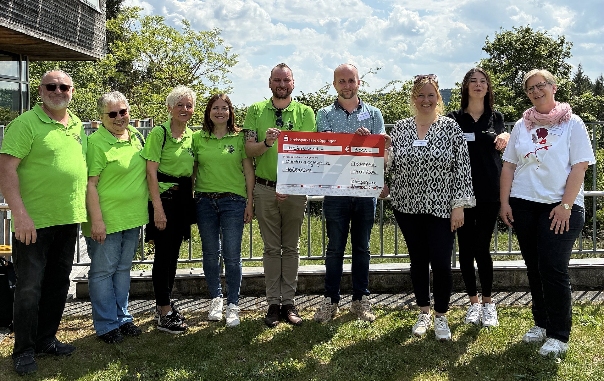 Scheckübergabe. Menschen stehen nebeneinander auf einer Wiese